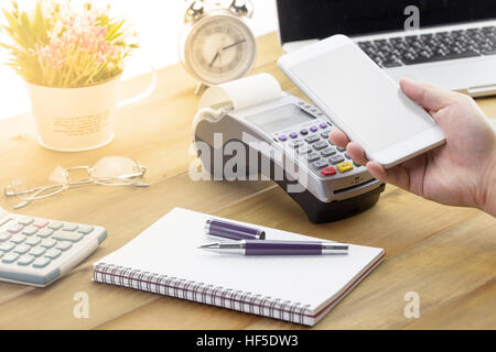 Hand holding mobile smart phone to made payment with credit card terminal or EDC. Customer pay by cellphone with empty screen. Stock Photo
