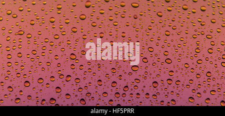 Water drops on a metallic surface with a pink to orange and yellow gradient Stock Photo