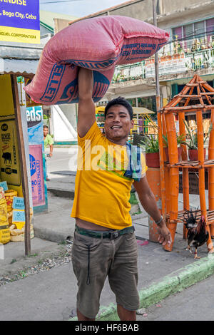 A Filipino teenage boy holds a 50-pound sack of white rice over his head with one arm in Bogo City, Cebu Island, Philippines. Stock Photo