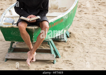 Man reading a book sitting on fishing boat on beach Stock Photo