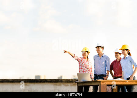 Multiethnic diverse group of engineers or business partners at construction site, pointing toward copy space on sky during sunset, engineering industr Stock Photo