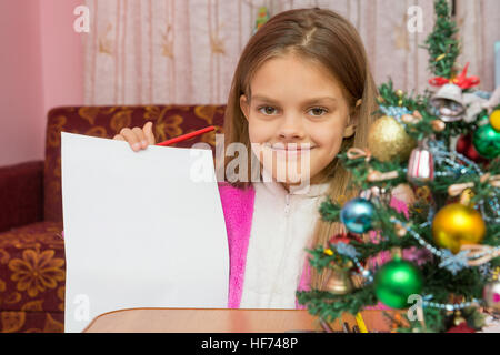 Happy girl shows a sheet of paper at a table in a Christmas setting Stock Photo