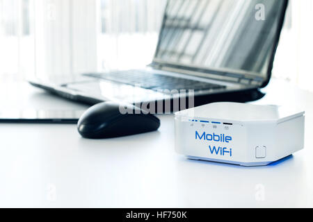 Mobile WiFi router device on the table and notebook on background Stock Photo