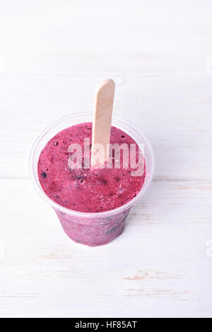 Blackcurrant popsicle made in plastic cup on white wooden background Stock Photo