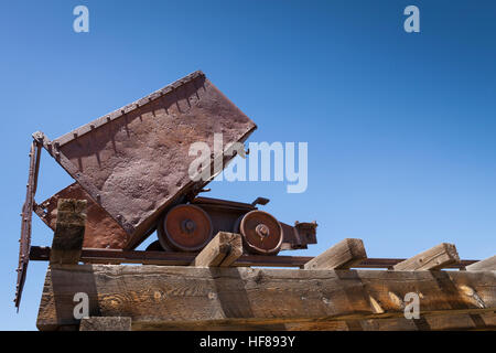 Old rusty mining ore cart on trestle under blue sky. Stock Photo