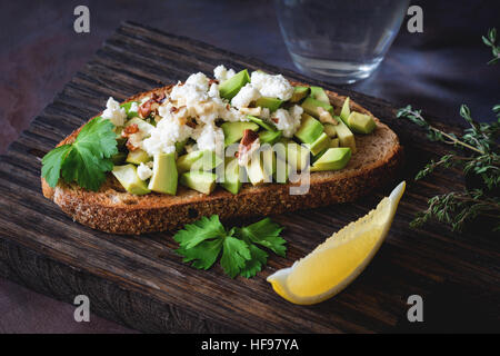 Healthy snack with avocado, white cheese, walnuts and olive oil on toasted whole grain bread. Close up view, selective focus Stock Photo