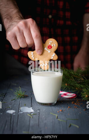 Gingerbread cookie and milk. Man holding gingerbread man cookie and going to sink it into glass of milk. Christmas food art Stock Photo