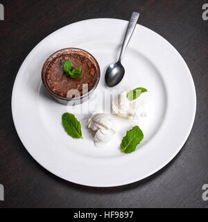 Warm dessert chocolate fondant lava cake served with vanilla ice cream balls and mint on white plate. Famous French dessert on dark wooden table top view Stock Photo