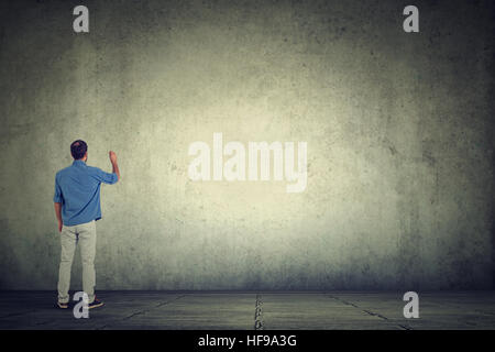Young student man writing something on a large empty gray wall Stock Photo