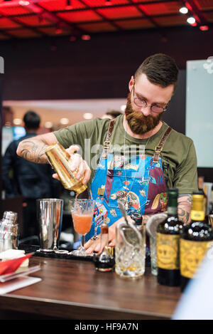 Kyiv, Ukraine - 30 october, 2016: Barman festival. Handsome bearded hipster with long beard and mustache holding shaker, making alcoholic cocktail. Stock Photo