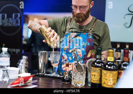Kyiv, Ukraine - 30 october, 2016: Barman festival. Handsome bearded hipster with long beard and mustache holding shaker, making alcoholic cocktail. Stock Photo