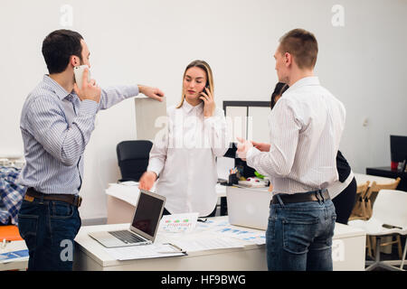 Group of four diverse cheerful co-workers taking self portrait and making funny gestures with hands at small office Stock Photo