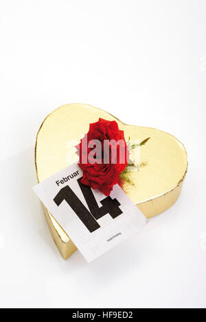 Golden heart-shaped gift box with a red rose and calendar page marking February 14th, Valentine's Day Stock Photo