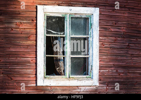 Broken window on an old red wooden house. Wooden debris inside. Stock Photo