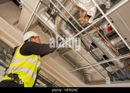 Engineer fitting air conditioning to office interior ceiling in commercial building Stock Photo