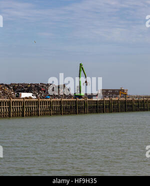 Scrap yard full of crushed cars and the crane with a claw that moves them into a huge pile. By the waterside at Newhaven. Stock Photo