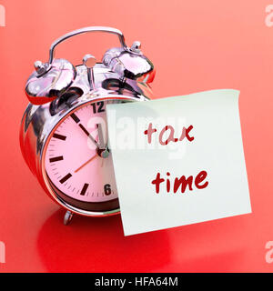 clock on a red table with sticker on it with words Tax Time Stock Photo