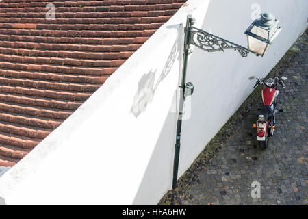 Motorcycle parked against a white wall with lantern and ancient roof on copper stone street viewed from above Stock Photo