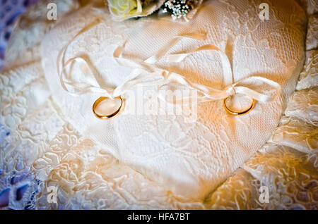 Double gold rings tied on a white pillow white heart-shaped Stock Photo