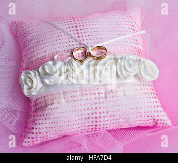 Double gold rings tied on a pink pillow with white roses Stock Photo