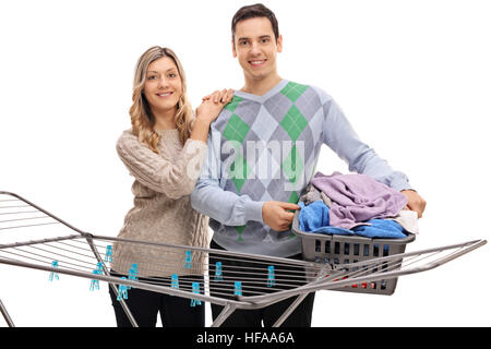 Happy couple standing behind a clothing rack dryer with the man holding a laundry basket full of clothes isolated on white background Stock Photo