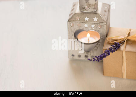 Gift box with a lavender twig, heart shaped candle holder with burning tea light on white background in contre jour Stock Photo