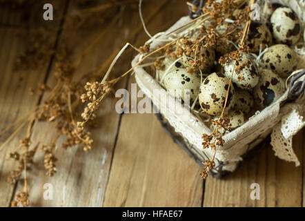 Quail eggs in lined wire basket, on straw, with beige dry flowers on barn wood background, Easter, rustic vintage style, kinfolk Stock Photo