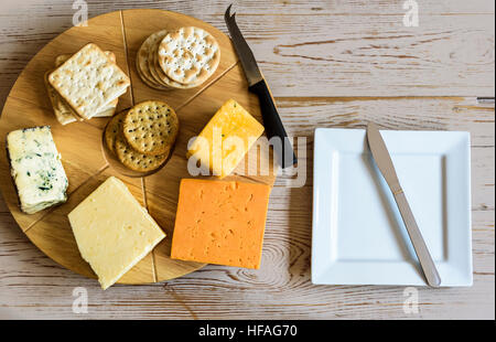Selection of cheeses on a round cheese board, sitting on an old table. Stock Photo