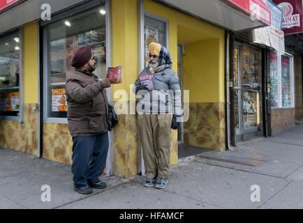 Two men in turbans who distribute advertising fliers conversing on a street corner in Jackson Heights, Queens, New York. Stock Photo