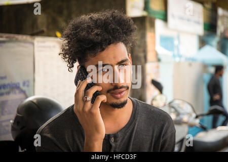 Handsome and attractive young Indian man with black fashionable curly hair and a black tshirt is talking on the phone Stock Photo
