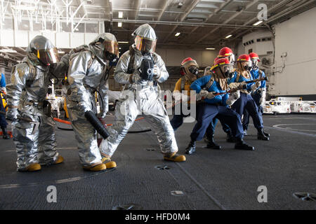 Sailors aboard the aircraft carrier USS Harry S. Truman (CVN 75) conduct a general quarters drill in the hangar bay. Aviation Boatswain’s Mate operates a naval firefighters thermal imager while deck department Sailors manage a fire hose, practicing emergency fire response procedures. Stock Photo
