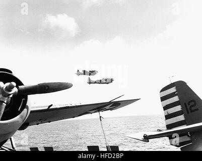 Two Douglas SBD-3 Dauntless scout bombers of Scouting Squadron Five (VS-5) fly past the ship, during operations in the Coral Sea, circa April 1942. Planes parked on the flight deck, in the foreground, are Grumman F4F-3 Wildcat fighters of Fighting Squadron 42 (VF-42).  Official U.S. Navy Photograph, now in the collections of the U.S. National Archives. SBD Dauntless of VS-5 fly past USS Yorktown (CV-5) in April 1942 Stock Photo