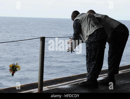 U.S. Navy Chief (select) Aviation Boatswain's Mates (Handling) Nnamdi Emenogu, left, and Troy Tracy honor the victims of the Sept. 11, 2001, attacks by casting flowers into the sea as part of a 9/11 remembrance ceremony in the hangar bay of the newly commissioned amphibious assault ship USS America (LHA 6) Sept. 11, 2014, in the Pacific Ocean. Terrorists hijacked four passenger aircraft Sept. 11, 2001. Two of the aircraft were deliberately crashed into the World Trade Center in New York; one was crashed into the Pentagon; the fourth crashed near Shanksville, Pa. Nearly 3,000 people died in the Stock Photo