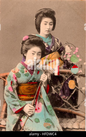 Circa 1900 sepia Japanese postcard. Women, geisha sitting golding sprig . Hand-coloured. Stock Photo