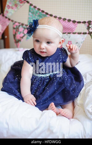 little girl in blue dress sits on the bed Stock Photo