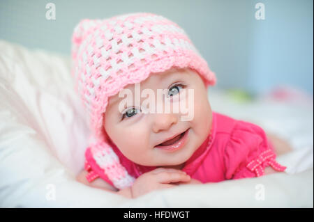 little girl in a knitted hat lying on the bed Stock Photo