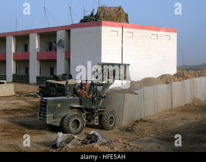 041027-N-5386H-005  Al Anbar Province, Iraq (Oct. 27, 2004) - Navy Reserve Seabee Equipment Operator 2nd Class Christopher Borchert, assigned to Naval Mobile Construction Battalion Two Three (NMCB-23), loads dirt into sandbag barriers surrounding a building at a Coalition Forces camp in Al Anbar Province, western Iraq. Known by the brand name Hessco, the barriers are a common site at military camps throughout Iraq, providing concealment and force protection. U.S. Navy photo by PhotographerÕs Mate 2nd Class Michael D. Heckman (RELEASED) US Navy 041027-N-5386H-005 Navy Reserve Seabee Equipment O Stock Photo