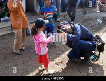 050114-N-2560Y-154 Banda Aceh, Sumatra, Indonesia (Jan. 14, 2005) - Photographer's Mate 3rd Class Tyler Clements, assigned to USS Abraham Lincoln (CVN 72), takes a photograph of a young Indonesia girl. The little girl is waiting with her family for an airlift to another area of Indonesia not affected by the recent Tsunami that devastated the Indonesian area of Banda Aceh on the island of Sumatra, Indonesia. U.S. Military personnel are assisting local authorities using helicopters to transport supplies, bringing in disaster relief teams, and to support humanitarian airlifts to tsunami-stricken  Stock Photo