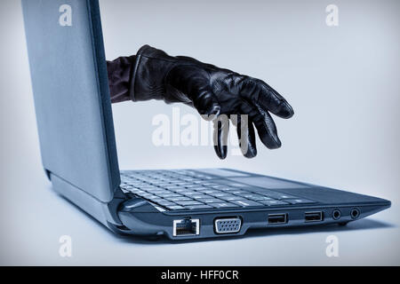 A gloved hand reaching out through a laptop, signifying a cybercrime or Internet theft while using Internet media. Stock Photo
