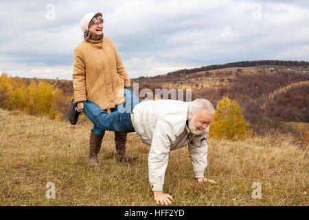 Elderly couple having fun and playing the wheelbarrow in nature.  'Woman carried his husband until old age.' Stock Photo