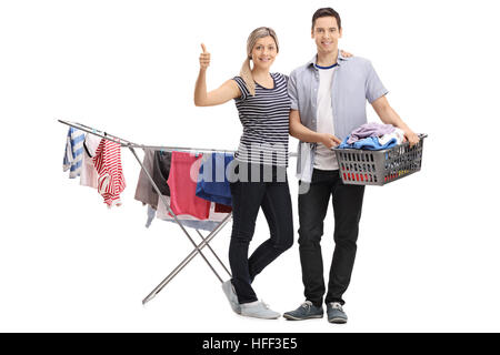 Full length portrait of a woman giving a thumb up with a guy holding a laundry basket in front of a rack dryer isolated on white background Stock Photo