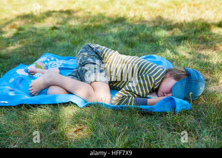 Child sleeping on a blue blanket on grassy ground at a campground in Vermont, USA. Stock Photo