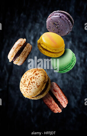 Assorted multi flavored macaroons floating against dark background Stock Photo