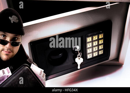 Thief holding a briefcase stuffed with cash, safe in background (composing shot) Stock Photo