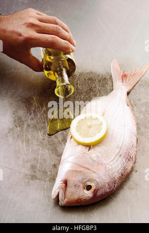 Raw gilt-head sea bream on a teppan grill plate, hand pouring olive oil Stock Photo