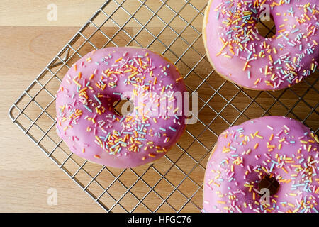 Closeup of Three Pink Doughnuts on Cooling Rack Stock Photo