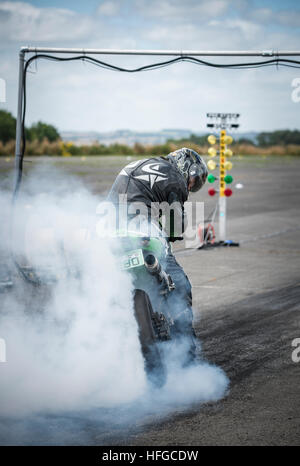 A motorcycle rider performs a burnout, to warm up the tire, before a drag racing event. Stock Photo