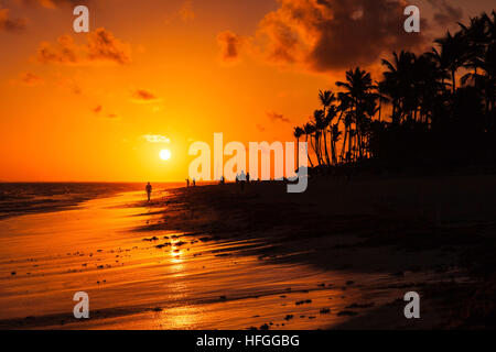 Sunrise over Atlantic ocean coast. Dominican republic, Punta Cana beach, ordinary people walking on sandy beach in red morning sunlight Stock Photo