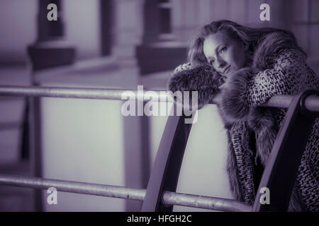 Photographic modeling as a career in the UK: A young slim attractive 20 year old caucasian woman girl with long blonde hair posing on seaside railings at dusk on a warm autumn evening, looking thoughtful and wistful, lonliness and sadness UK Stock Photo