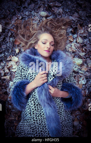 Photographic modeling as a career in the UK: A young slim attractive 20 year old caucasian woman girl with long blonde hair  lying  with her eyes closed on her back on the ground on a cold  frosty day looking like an Ice Queen Stock Photo